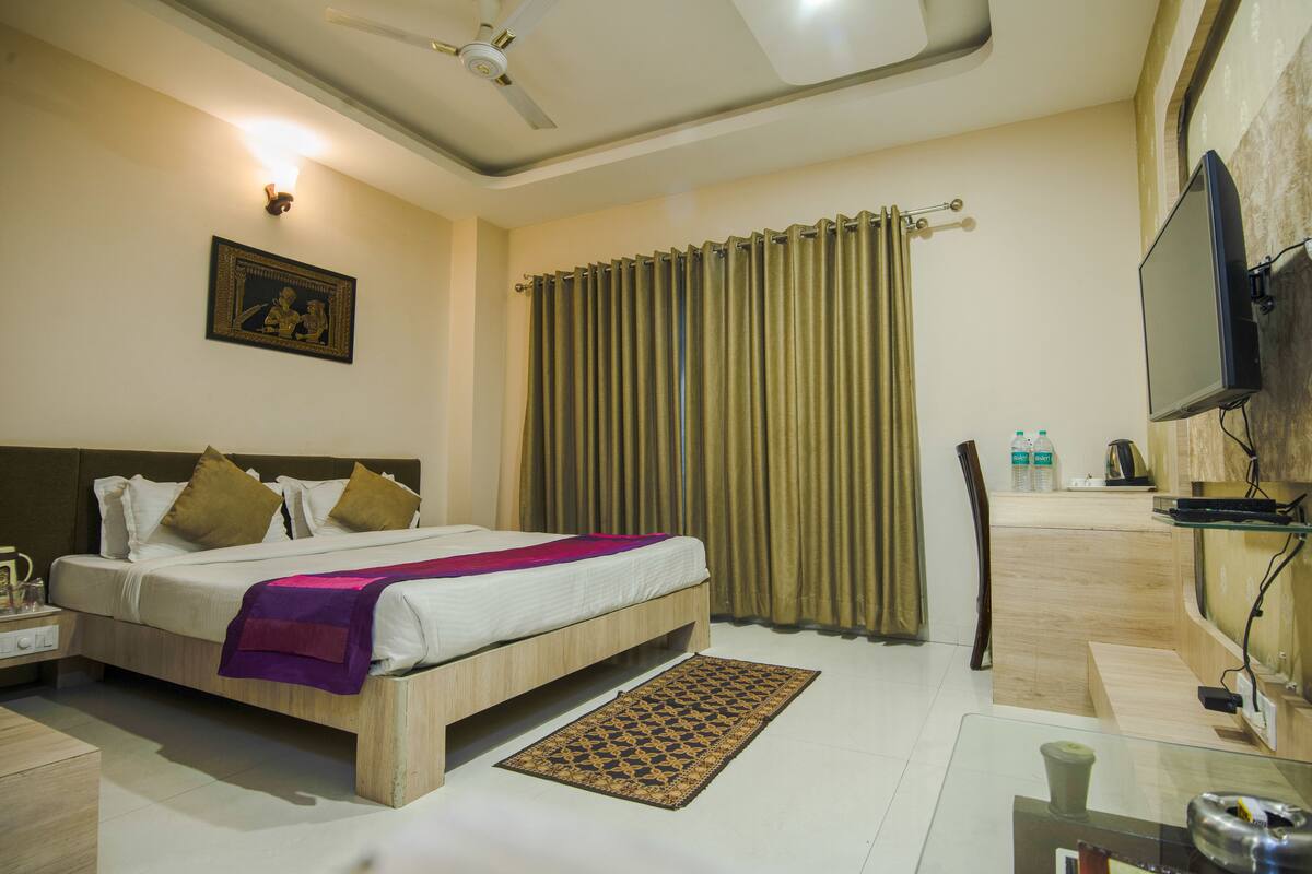 Quarto de hotel com cama, televisão, escrivaninha e área de banheiro.