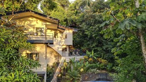 Una casa moderna de dos pisos con piscina, rodeada de abundante vegetación y árboles.