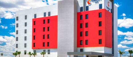 Un hotel Comfort Inn de varios pisos con fachada roja y blanca, estacionamiento y palmeras.