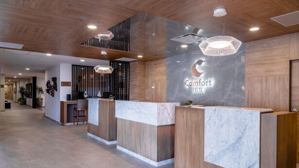 A hotel reception area with wooden reception desks, marble accents, and modern lighting fixtures. - Comfort Inn Hermosillo Aeropuerto (Hermosillo)
