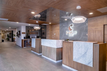 A hotel reception area with wooden reception desks, marble accents, and modern lighting fixtures.