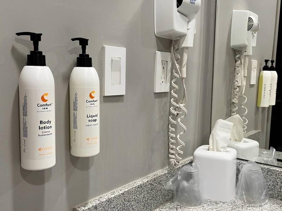 A bathroom with a mirror, a hairdryer, and toiletries including body lotion and liquid soap.