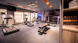 Un gimnasio moderno con máquinas de cardio, equipo de entrenamiento de pesas y un televisor montado en la pared.