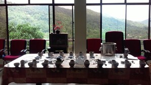 Un comedor con una mesa dispuesta para una comida, rodeado de sillas y grandes ventanales que ofrecen vistas a un paisaje montañoso.