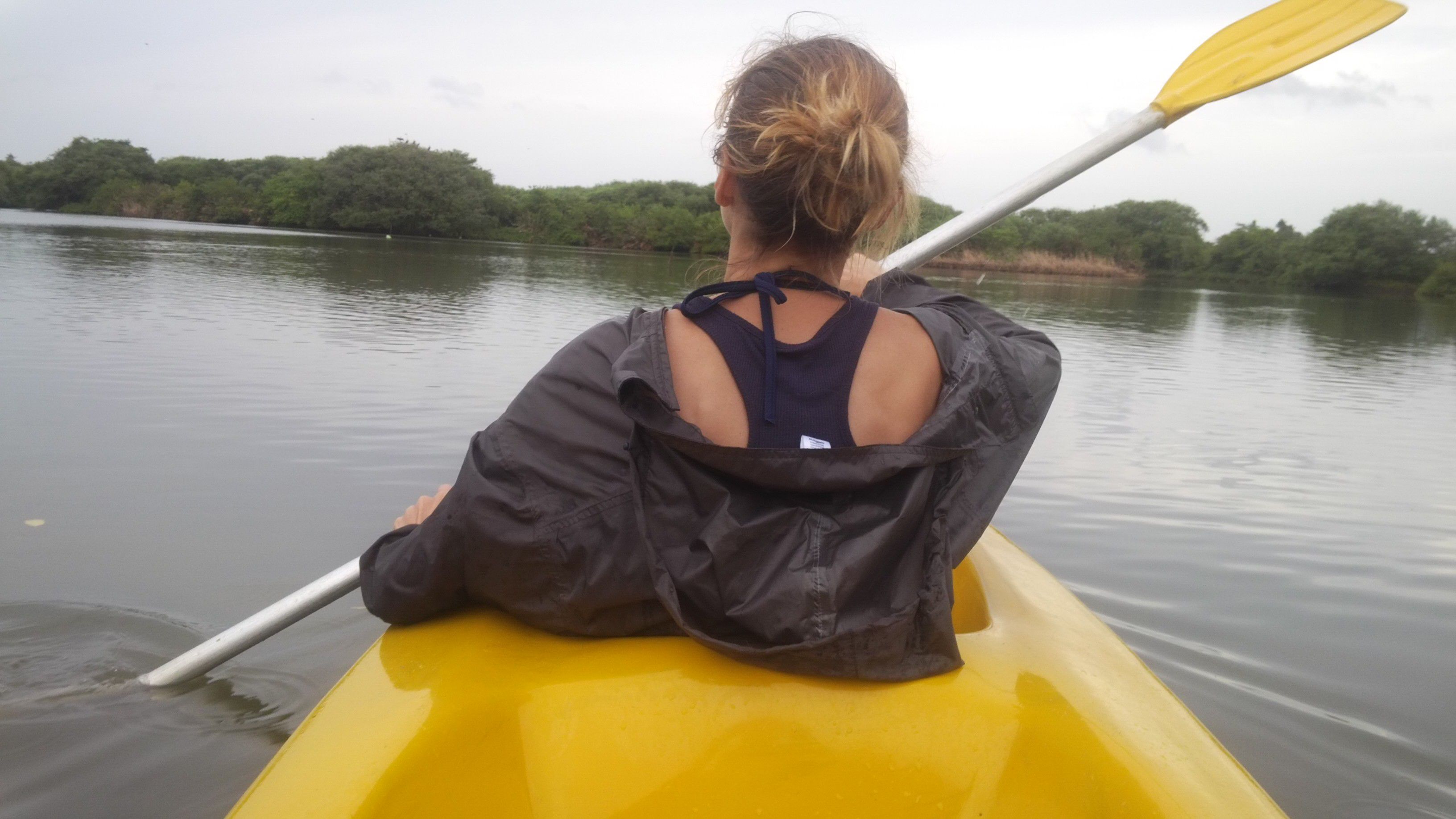 A person in a kayak on a calm body of water with trees in the background.