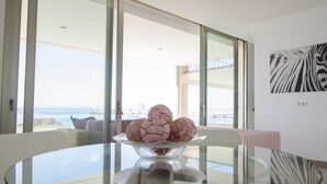 Una sala de estar moderna con una mesa de vidrio, un cuenco de objetos decorativos y vista al mar a través de amplias ventanas.