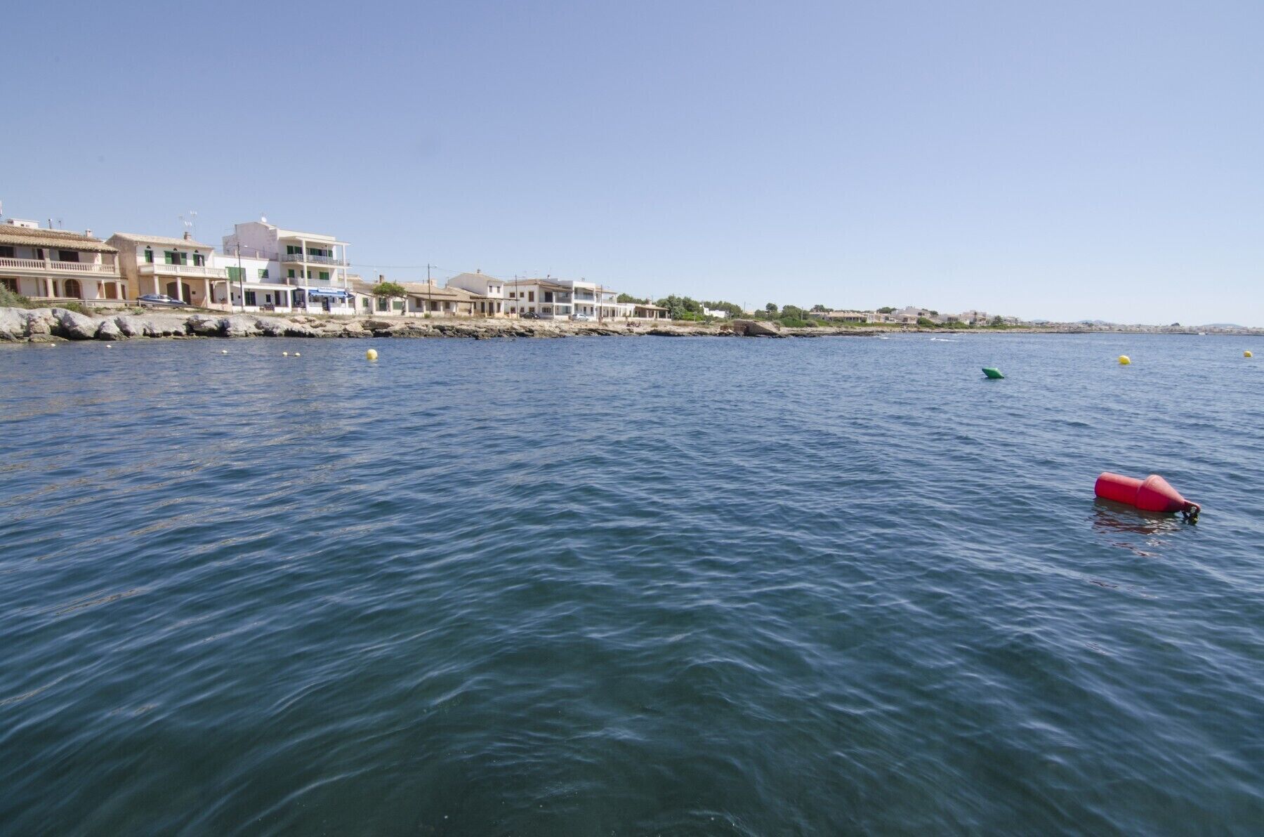 A coastal view with buildings along the shore and buoys in the water.