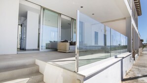 Un edificio moderno con balcón de vidrio, sofá de mimbre y una escalera que lleva a la entrada.