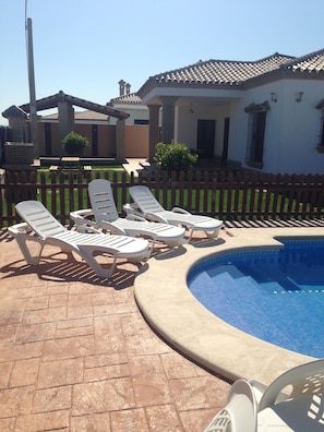 A swimming pool with lounge chairs and a brick patio.