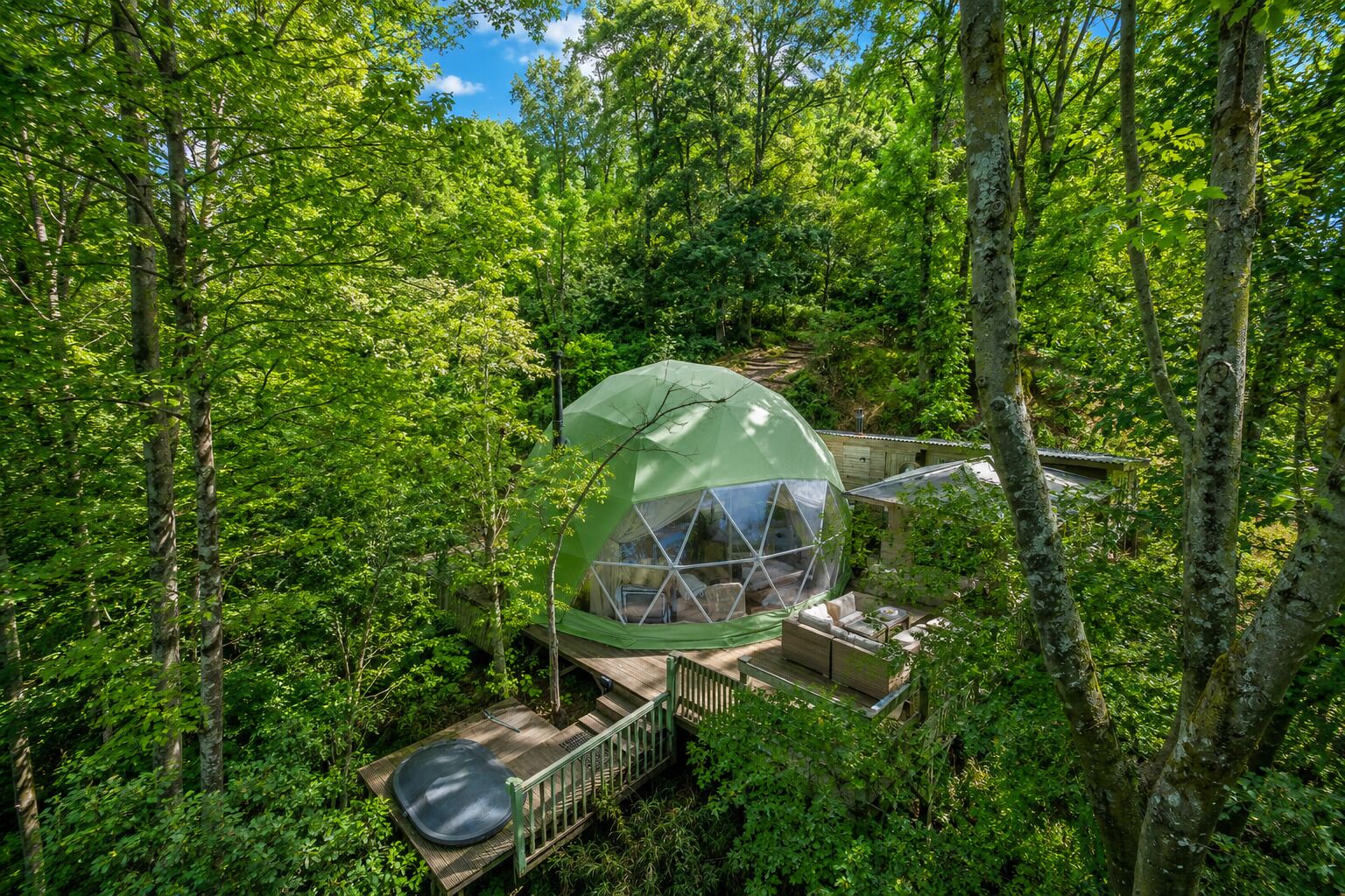 Une structure en forme de dôme géodésique, entourée d’une forêt dense.
