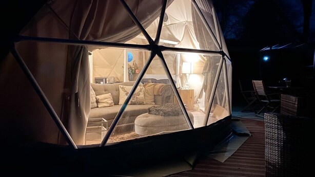 Eine geodätische Kuppelstruktur mit gemütlicher Einrichtung, inklusive Sofa, Kissen und Lampe.