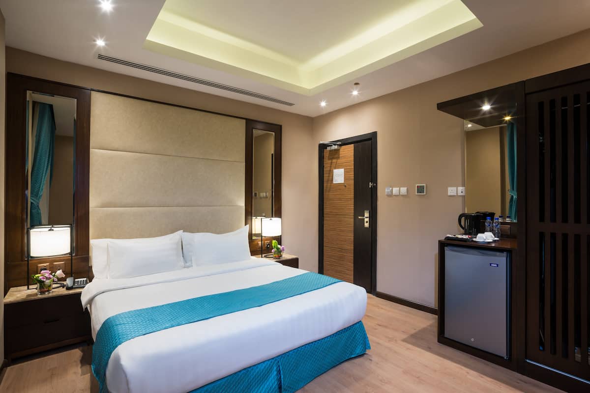 A hotel room with a large bed, bedside lamps, a minibar, and a ceiling light.
