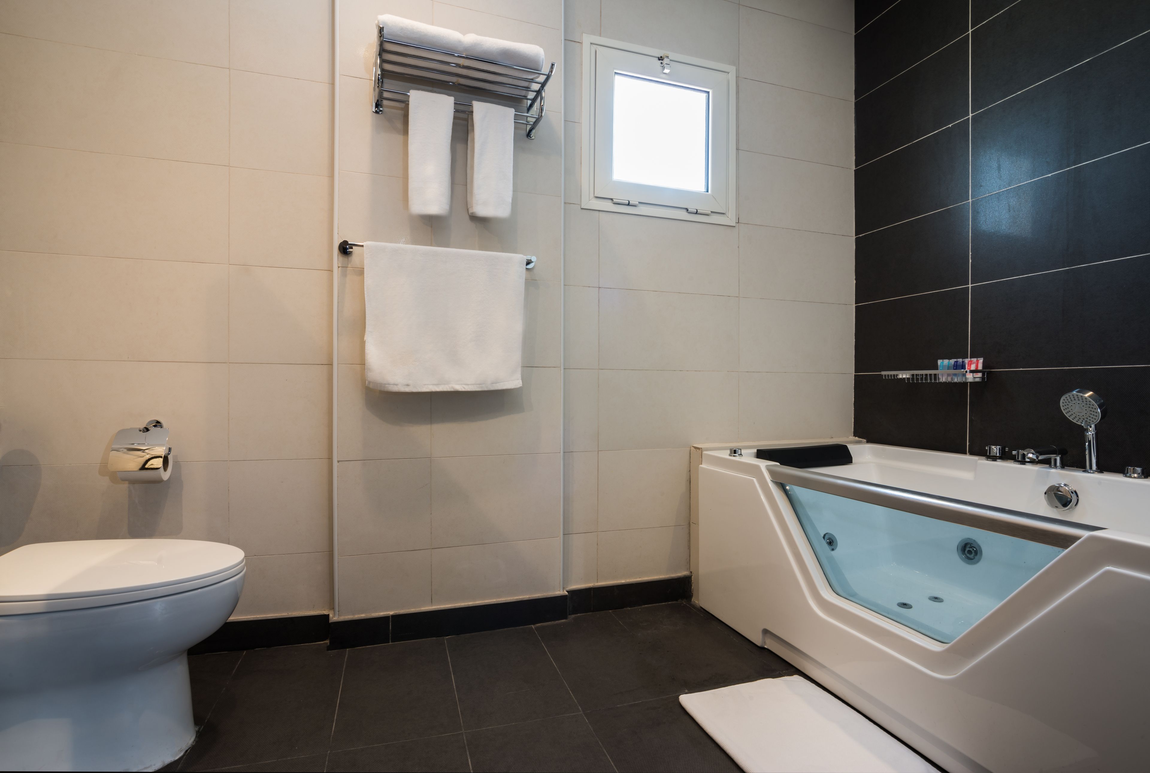 A modern bathroom with a toilet, a bathtub, and a window.