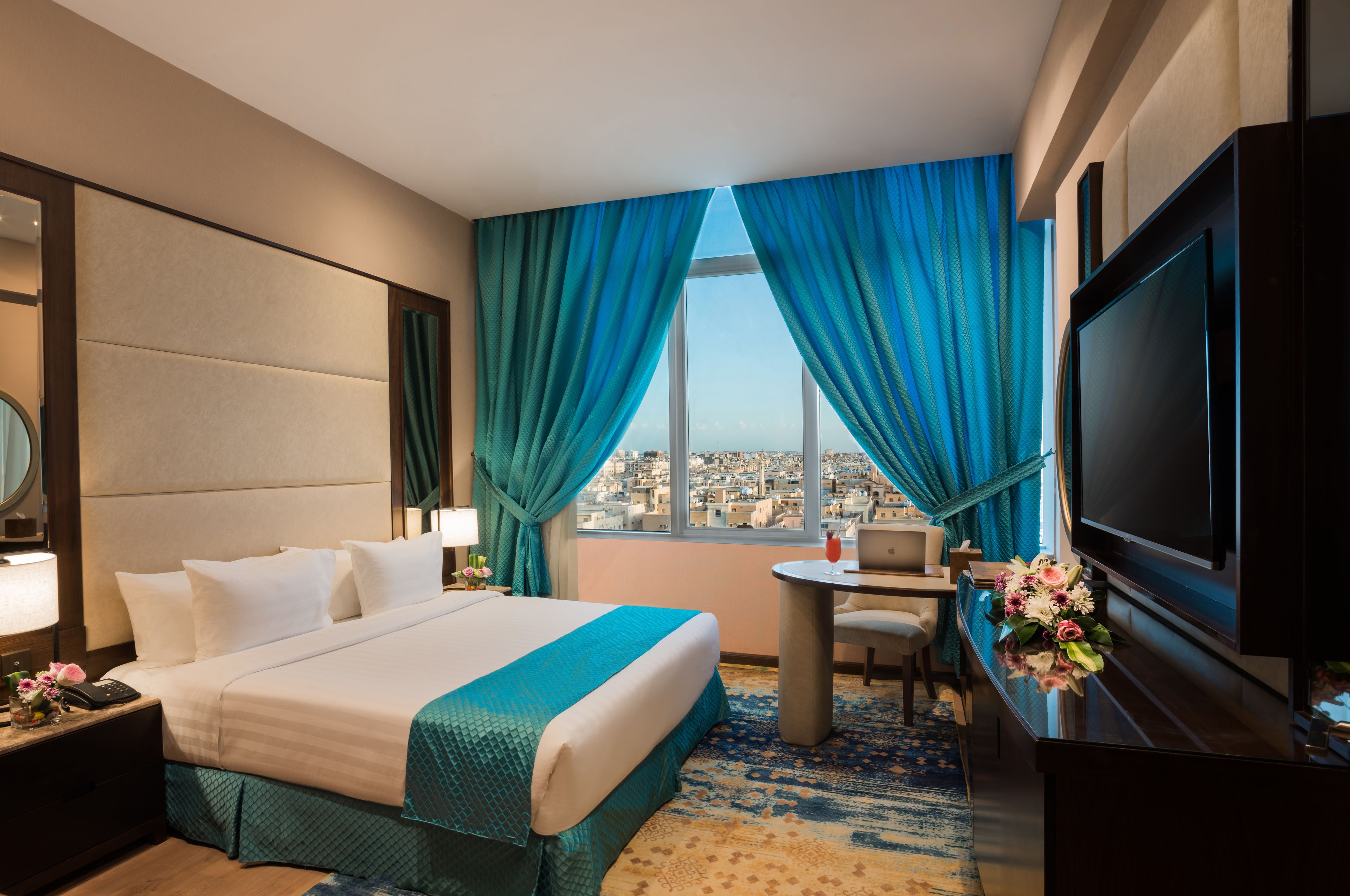 Habitación de hotel con cama, escritorio, televisor y vista a la ciudad.