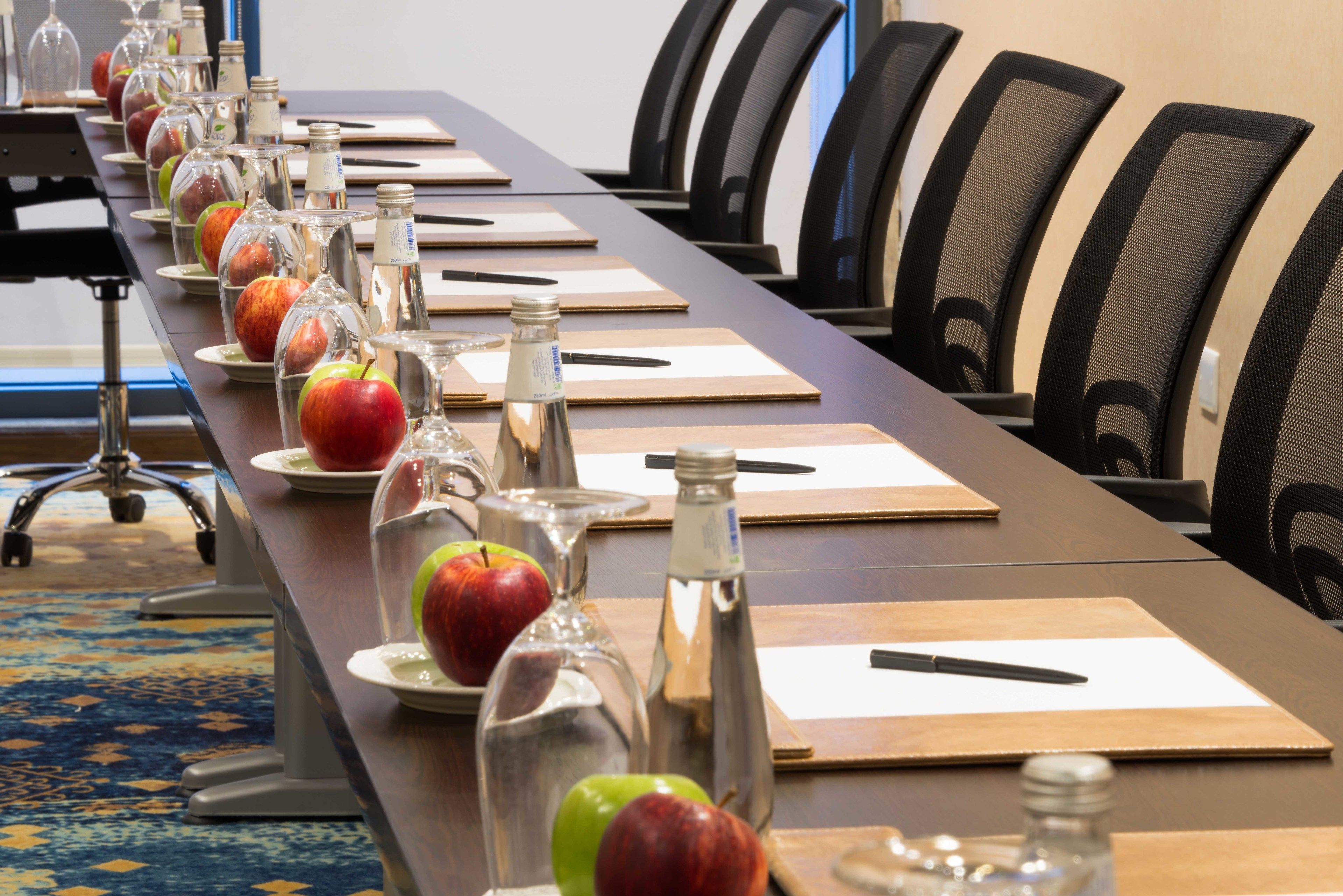 A conference table with apples, water bottles, and notepads in a meeting room.
