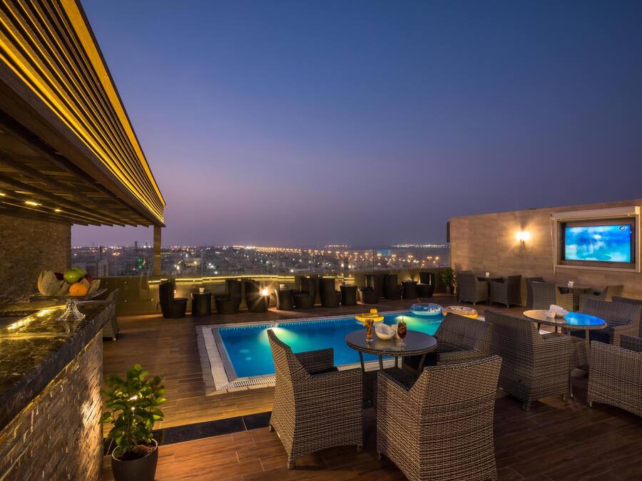 A rooftop bar with a pool, wicker furniture, and a TV screen.