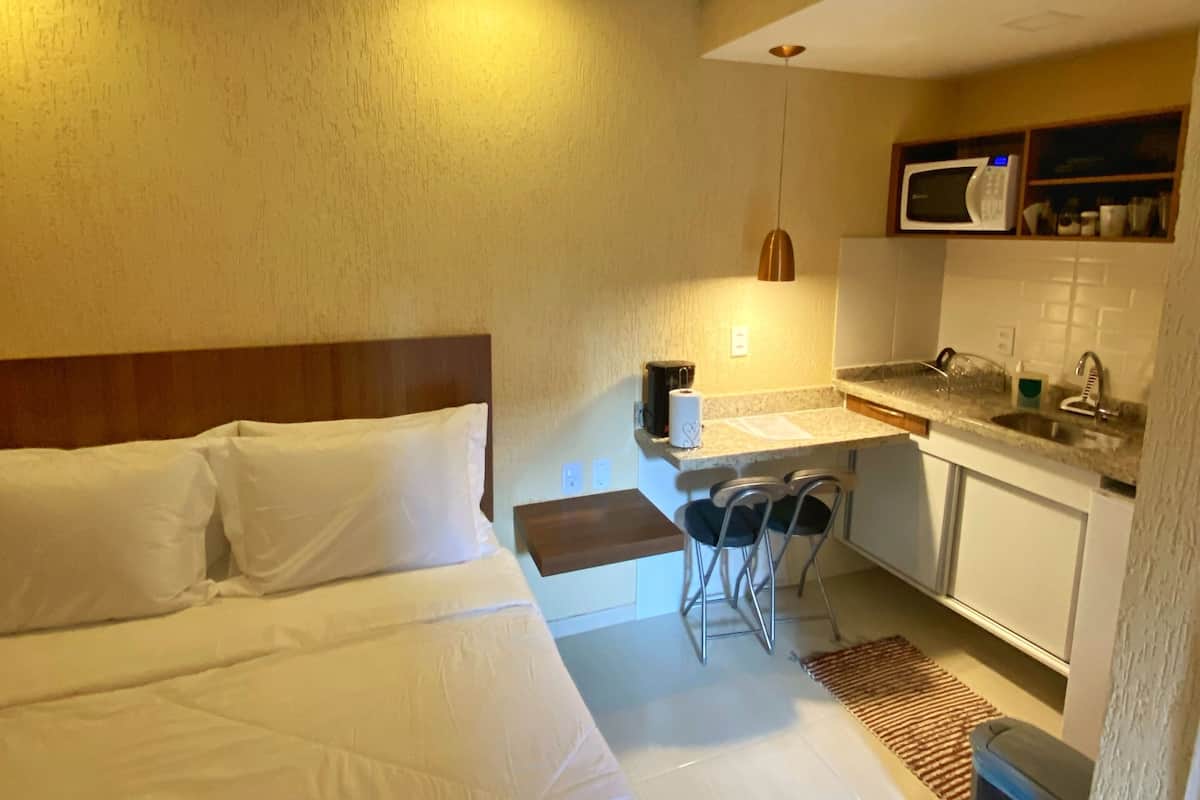 A hotel room with a bed, a small kitchenette, and a desk.