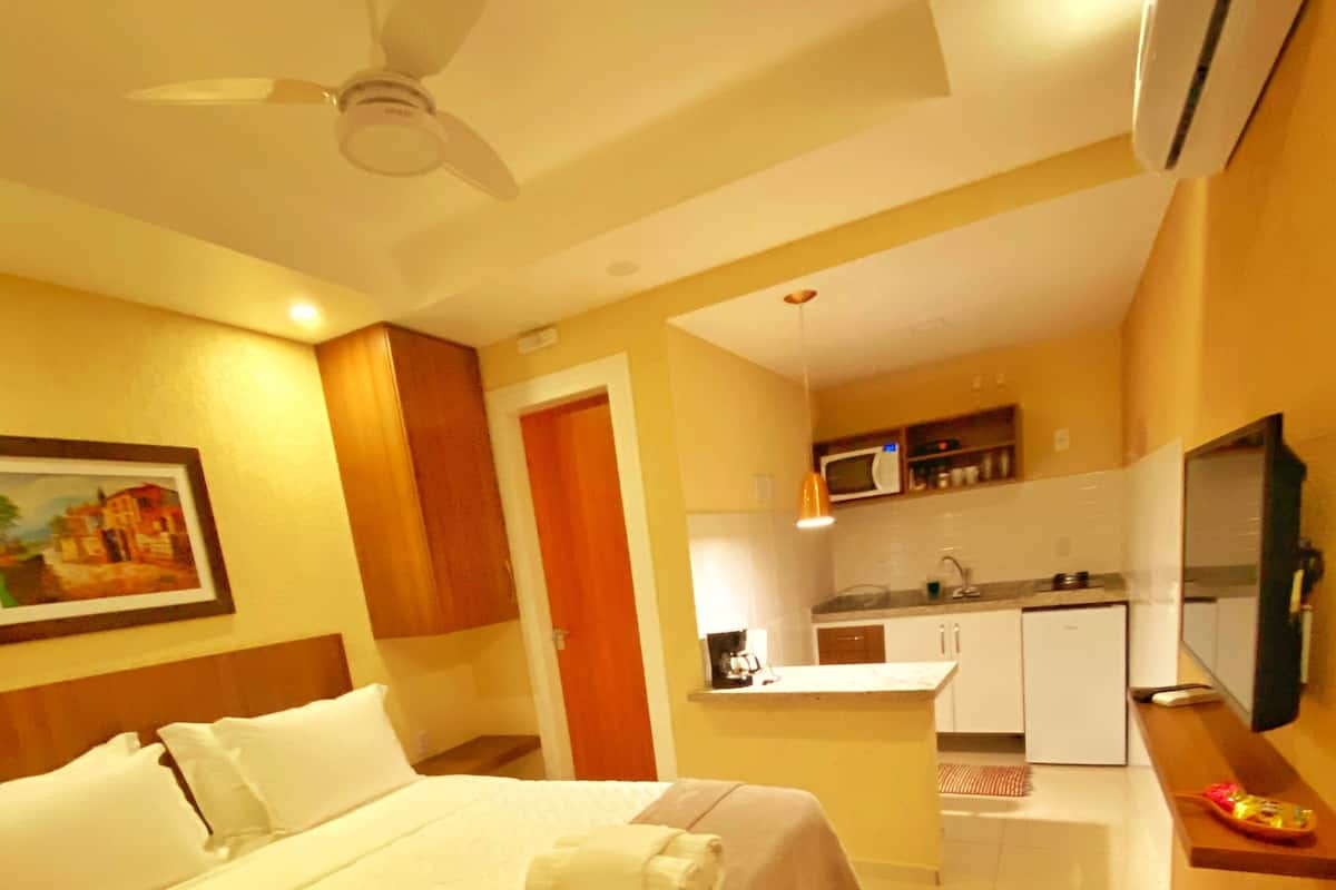 A hotel room with a bed, a ceiling fan, a microwave, a sink, and a small kitchen area.