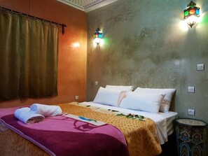 A hotel room with a bed, a nightstand, a wall-mounted light fixture, and a curtain. - Dar kaltoum (Ait Taguella)