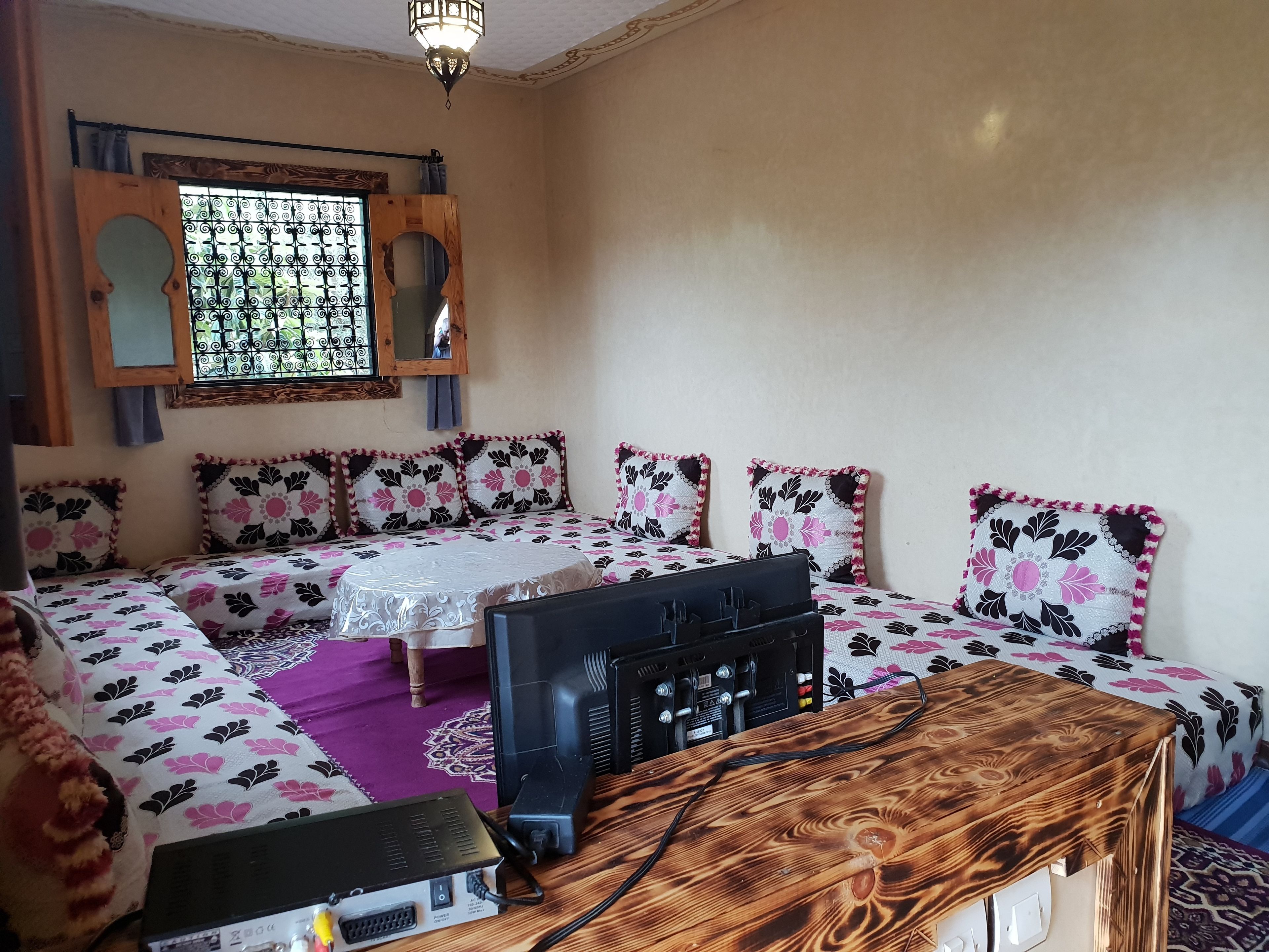Ein Schlafzimmer mit einem Bett, einem Holztisch, einem Fernseher und einem Fenster mit Verzierungen.