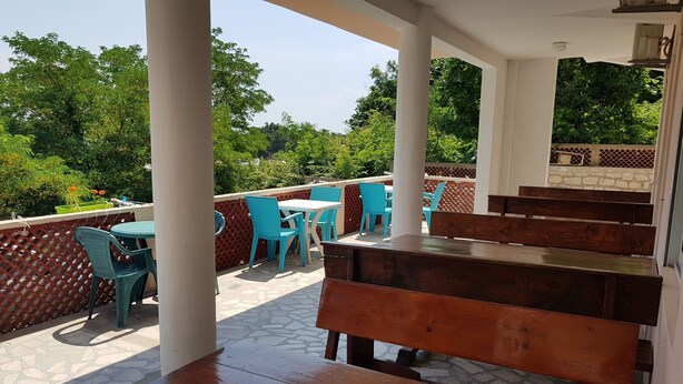 An outdoor patio with wooden benches and blue plastic chairs, surrounded by a lattice fence and greenery. - Economy double room - close to the Velika Plaza for cheap price (UL)