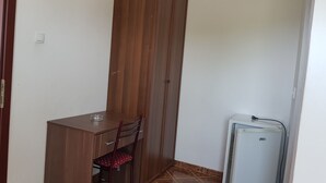A small room with a wooden desk, a chair, a wardrobe, and a white refrigerator. - Economy double room - close to the Velika Plaza for cheap price (UL)