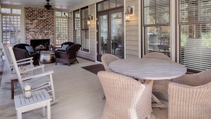 En overdækket terrasse med fletmøbler, et rundt bord og en murstenspejs.