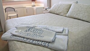 A neatly made bed with a quilted blanket and a towel with "Xiku's Palace Hotel" text. - Xikus Palace Hotel (Guanhaes)