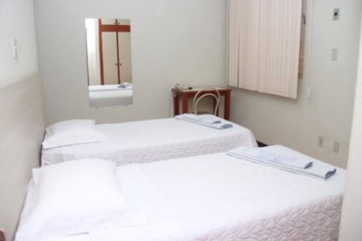 Habitación de hotel con dos camas individuales, un escritorio pequeño, una silla y un espejo en la pared.