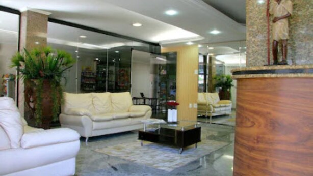 A modern lobby with a white sofa, a coffee table, and a statue on a pedestal. - Xikus Palace Hotel (Guanhaes)