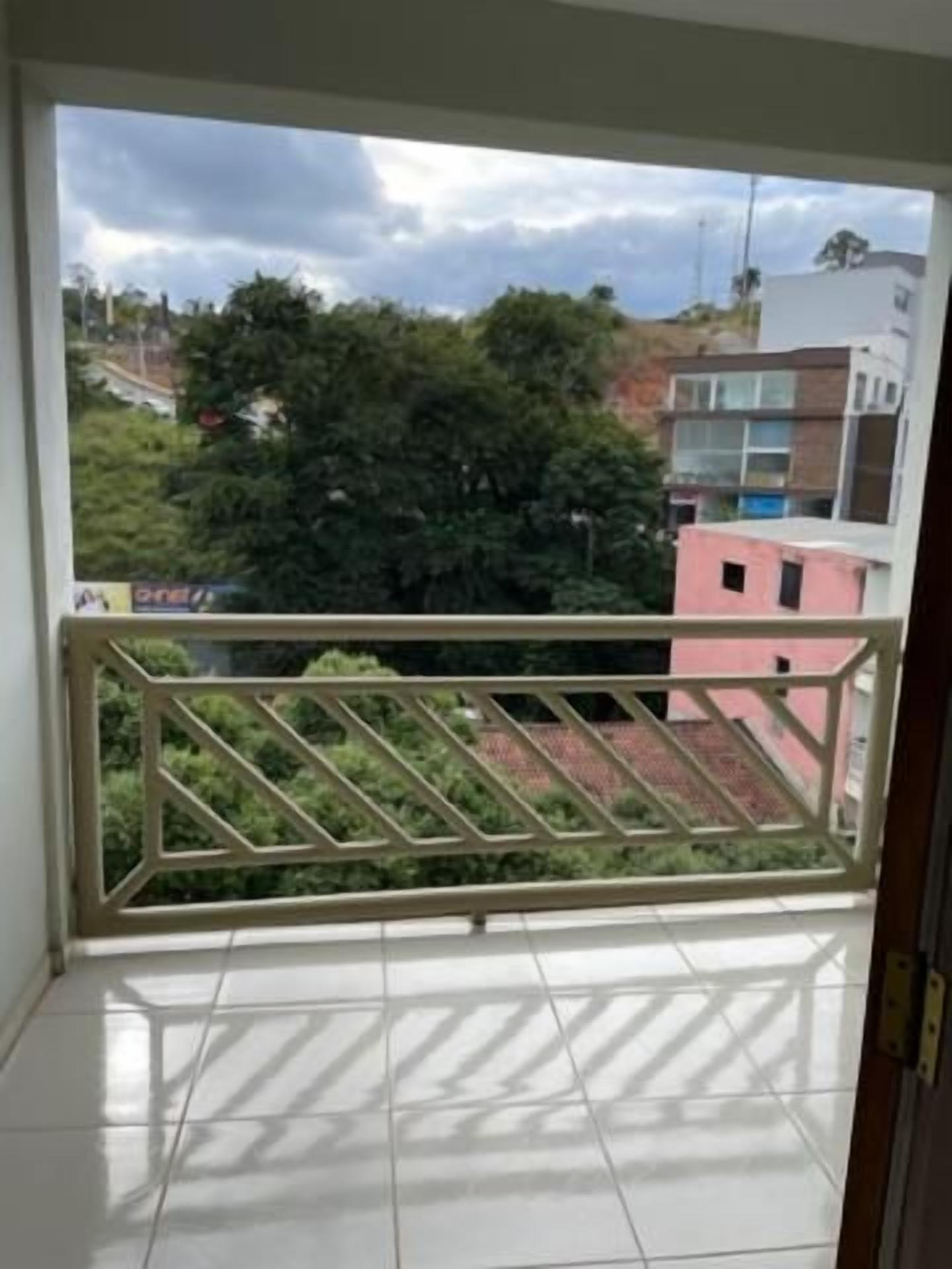Een balkon met een metalen hekwerk, een betegelde vloer en een uitzicht op gebouwen en bomen in de verte.