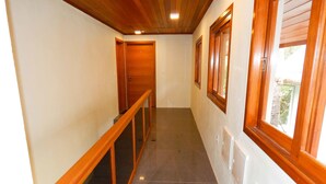 A narrow hallway with wooden doors, a glass railing, and a window with a view of greenery. - Flats Requinte Gramado (Gramado)