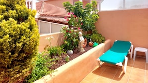 A patio with a green lawn, a white chair, a blue lounge chair, and a small white statue. - Casa "MANUELA" Feel at home in La Paz - Vivienda Vacacional (Puerto de la Cruz)