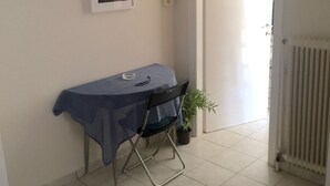 Una habitación con una mesa cubierta por un mantel azul, una silla, una planta en maceta y un radiador.