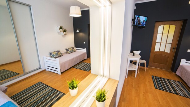 A modern room with a bed, a small table, a chair, a TV, and a door.