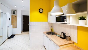 A modern kitchen with white cabinets, a yellow accent wall, a clock, and pendant lights.