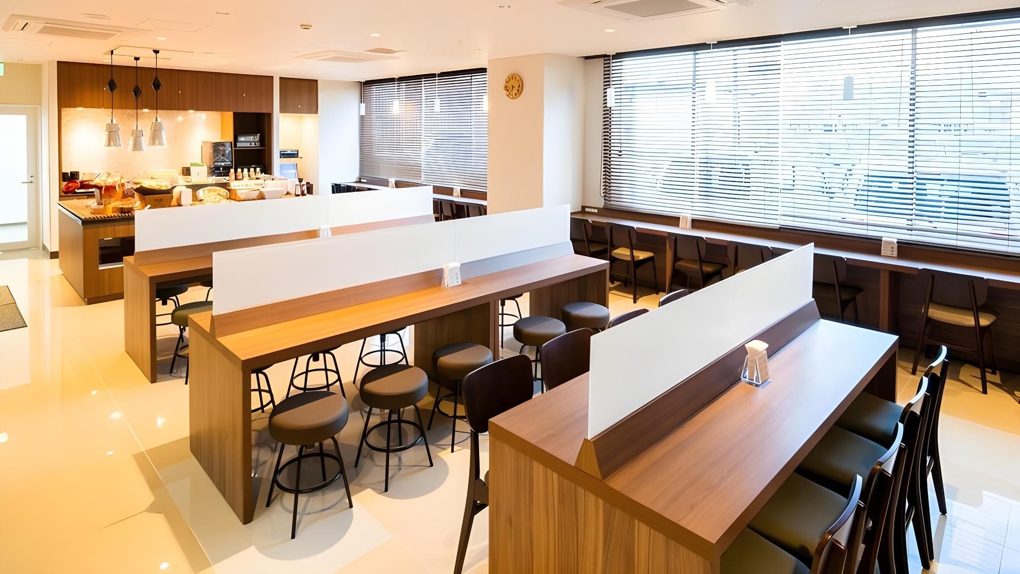 A modern bar area with high stools, a long counter, and a large window with blinds.