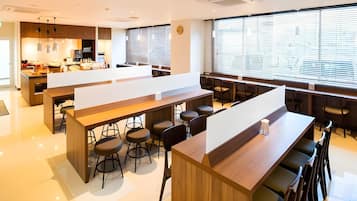 A modern bar area with high stools, a long counter, and a large window with blinds.