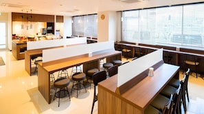 Un espace bar moderne avec des tabourets hauts, un long comptoir et une grande fenêtre équipée de stores.
