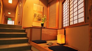Um interior japonês tradicional com escada, piso de esteiras de tatame, uma mesinha com luminária e um vaso de planta.