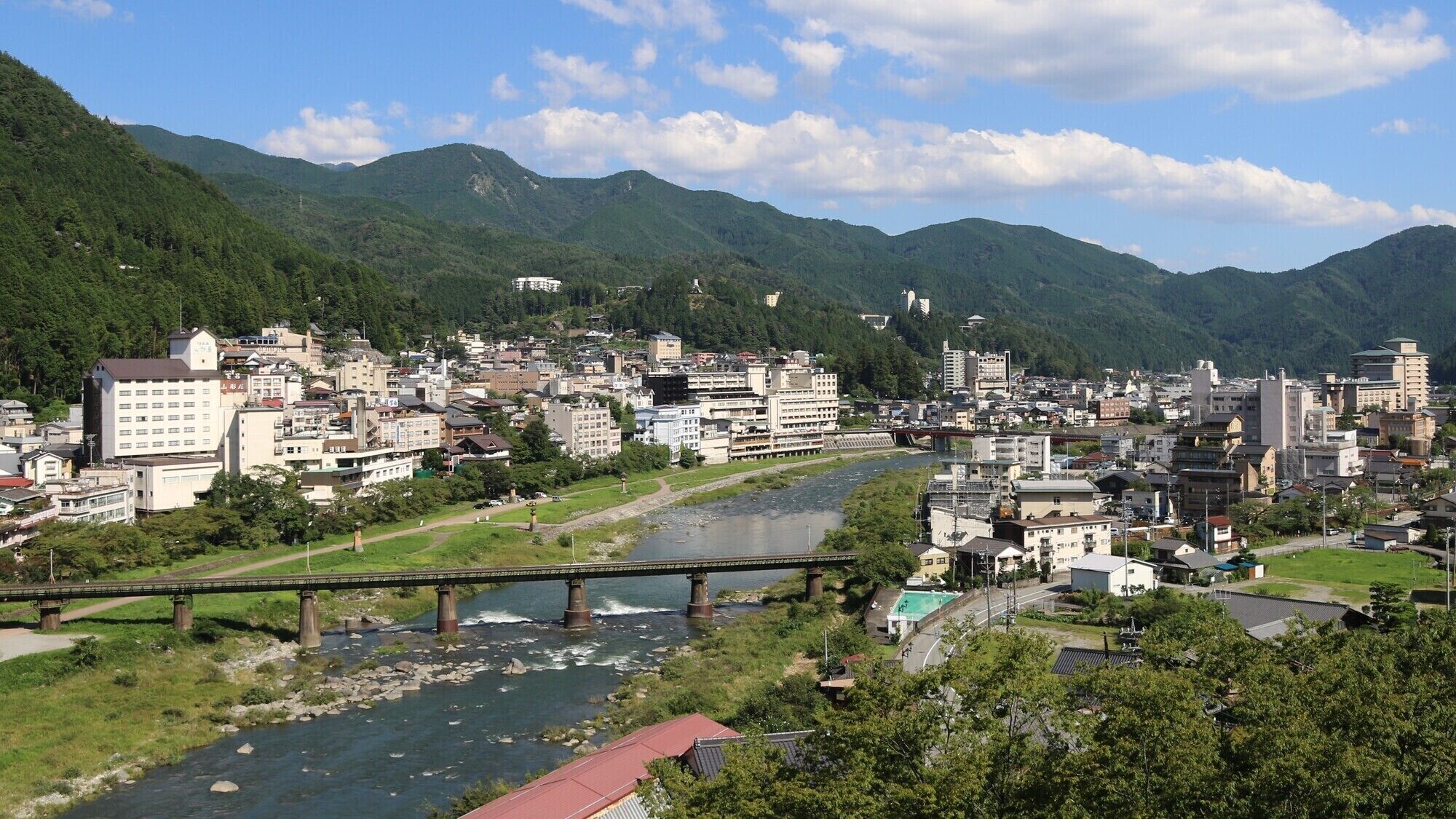 A riverside town with a bridge, buildings, and mountains in the background.