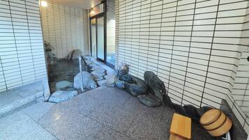 A traditional Japanese onsen with a stone pathway leading to a hot spring, tiled walls, and a wooden barrel.