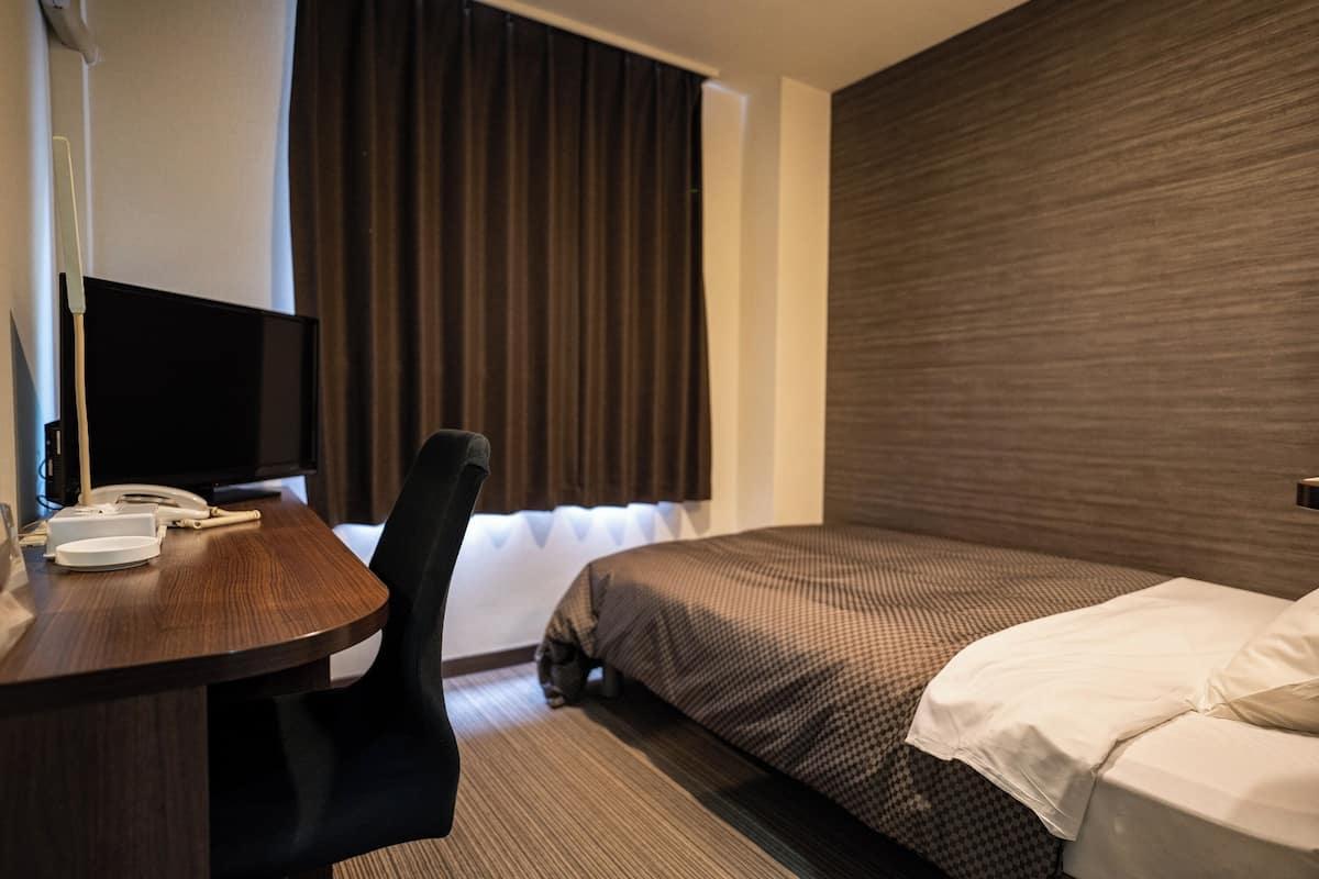 Een hotelkamer met een bed, een bureau, een stoel, een televisie en een raam met gordijnen.