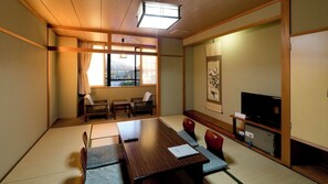 Una habitación japonesa tradicional con suelo de tatami, una mesa baja, sillas, un televisor y una puerta corredera.