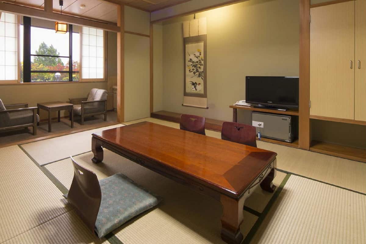 A traditional Japanese-style room with tatami flooring, a low table, chairs, a television, and a cabinet.