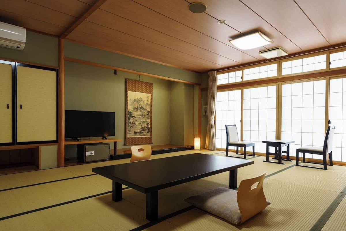 A traditional Japanese room with tatami flooring, a television, a painting, and sliding doors.