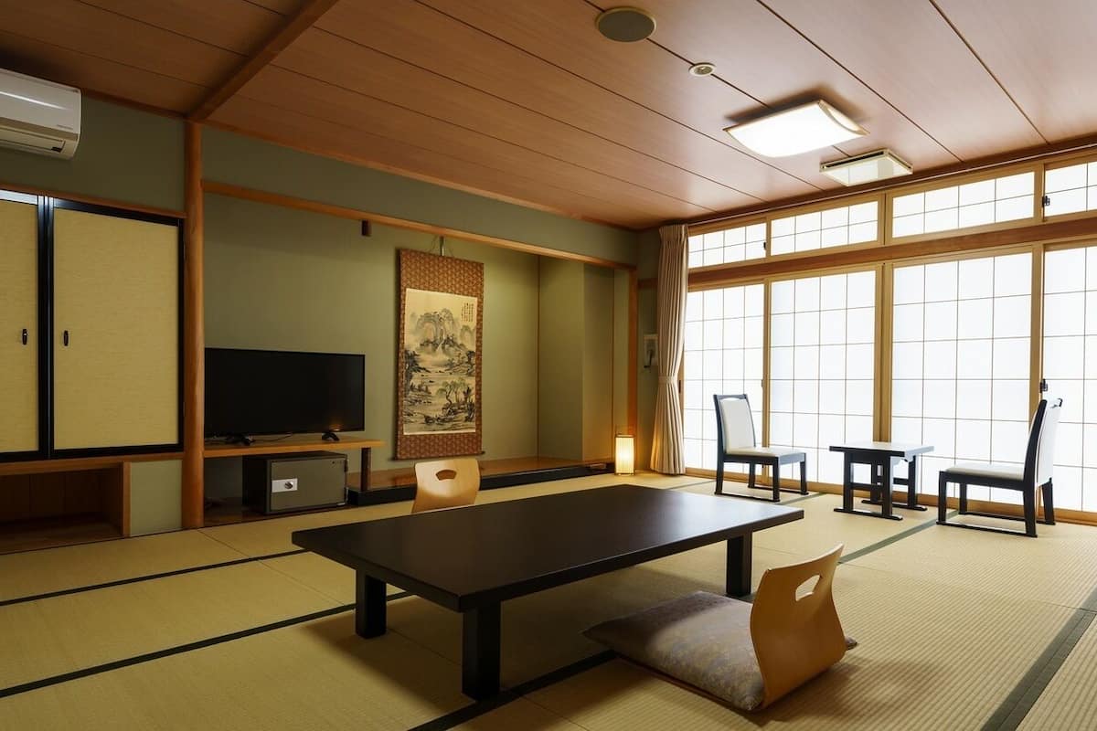 A traditional Japanese room with tatami flooring, a low table, chairs, a TV, and sliding doors.
