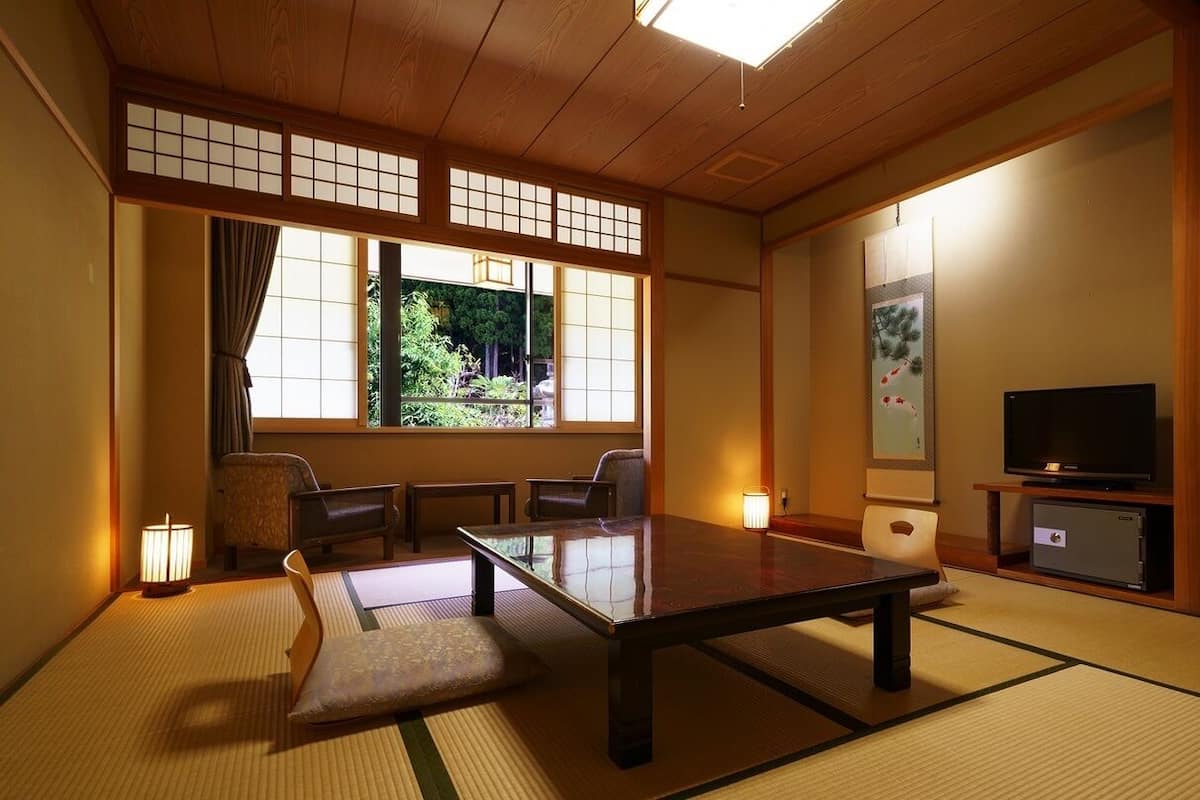 A traditional Japanese room with tatami flooring, a low table, seating, a TV, and a sliding door.