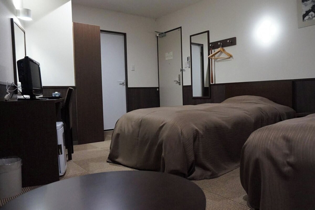 Habitación de hotel con dos camas, un escritorio con computadora, un espejo y un teléfono.