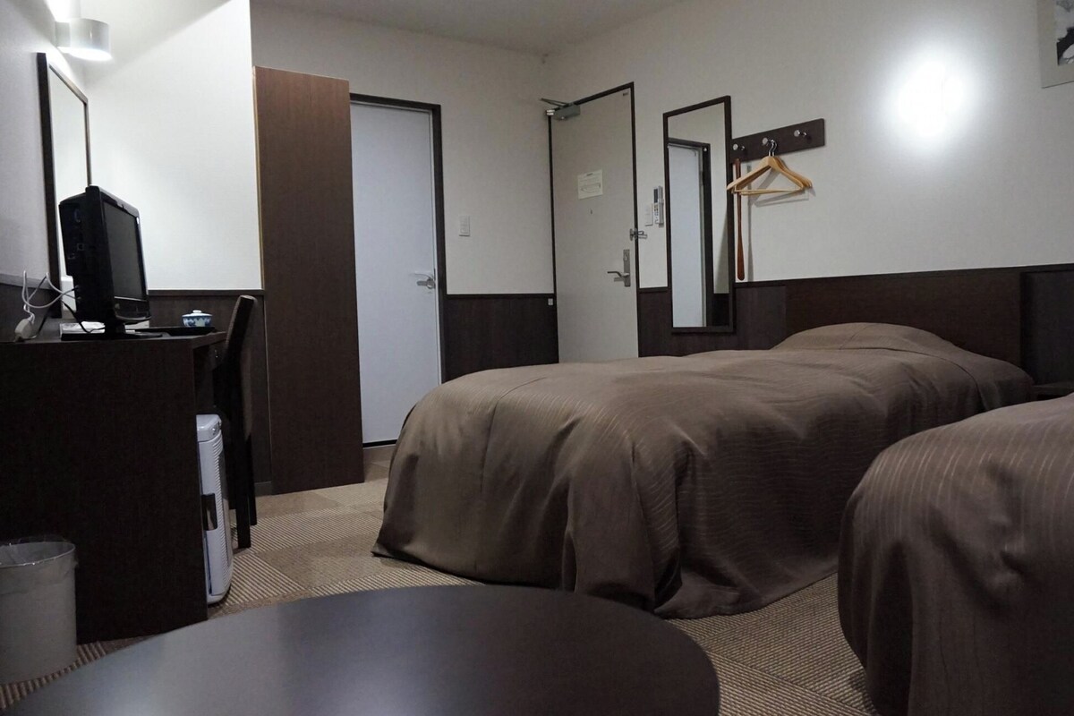 A hotel room with two beds, a desk with a computer, a telephone, and a mirror on the wall.
